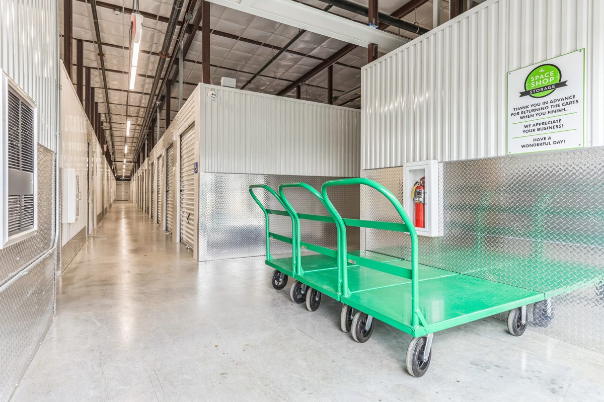 Clean, well-lit self storage units near me along a wide indoor corridor at a modern Thailand storage facility, with a trolley for moving items